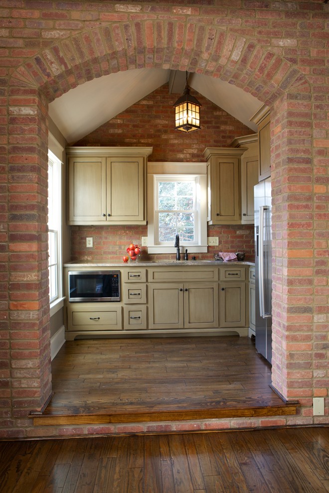 Klassisk inredning av ett avskilt, litet l-kök, med luckor med profilerade fronter, rostfria vitvaror, mörkt trägolv, en undermonterad diskho, granitbänkskiva och rött stänkskydd