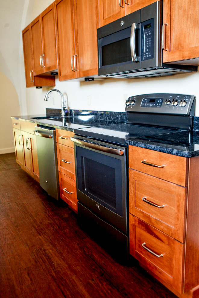 Exempel på ett amerikanskt kök, med en enkel diskho, luckor med upphöjd panel, skåp i mellenmörkt trä, granitbänkskiva, rostfria vitvaror och mörkt trägolv