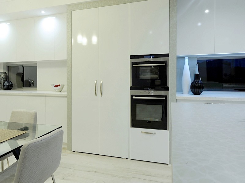 Large modern kitchen in Perth with a double-bowl sink, white cabinets, engineered stone countertops, white splashback, glass sheet splashback, black appliances, light hardwood flooring and an island.