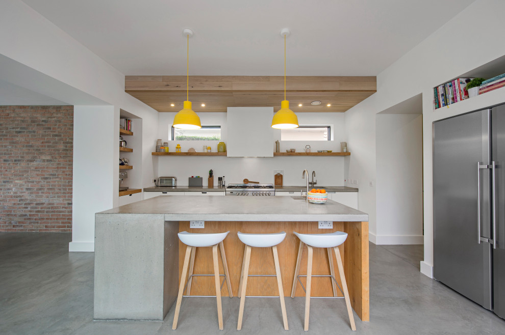 Design ideas for a medium sized contemporary open plan kitchen in Dublin with a built-in sink, flat-panel cabinets, white cabinets, concrete worktops, white splashback, stainless steel appliances, concrete flooring, an island, grey floors, grey worktops and a timber clad ceiling.