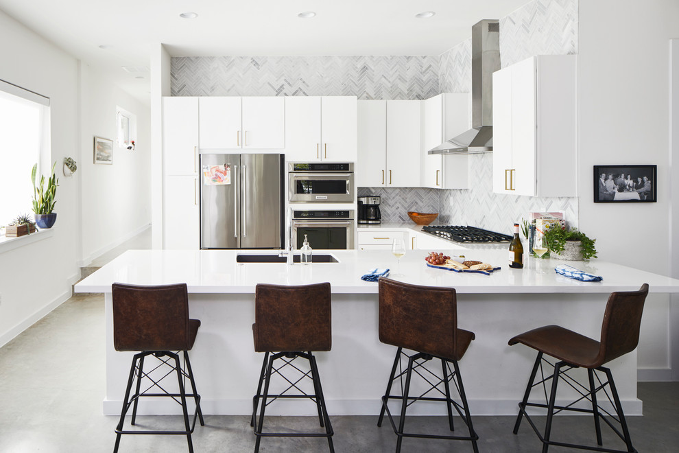 Cette image montre une cuisine design en U avec un évier encastré, un placard à porte plane, des portes de placard blanches, une crédence multicolore, un électroménager en acier inoxydable, sol en béton ciré et un sol gris.