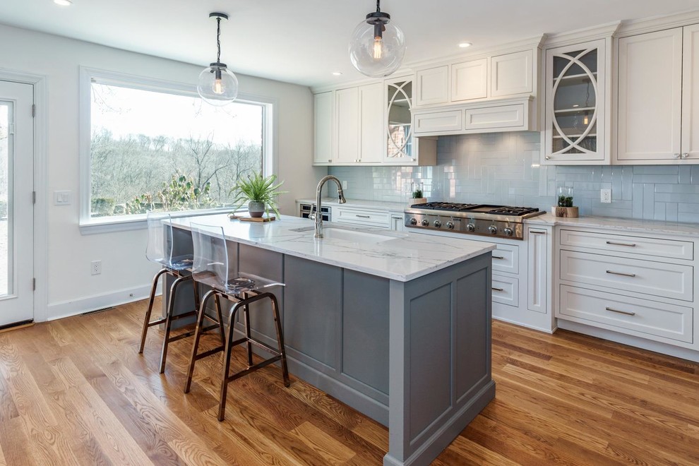 Classic kitchen in Cincinnati with a submerged sink, white cabinets, blue splashback, glass tiled splashback, stainless steel appliances, medium hardwood flooring, an island, white worktops and recessed-panel cabinets.