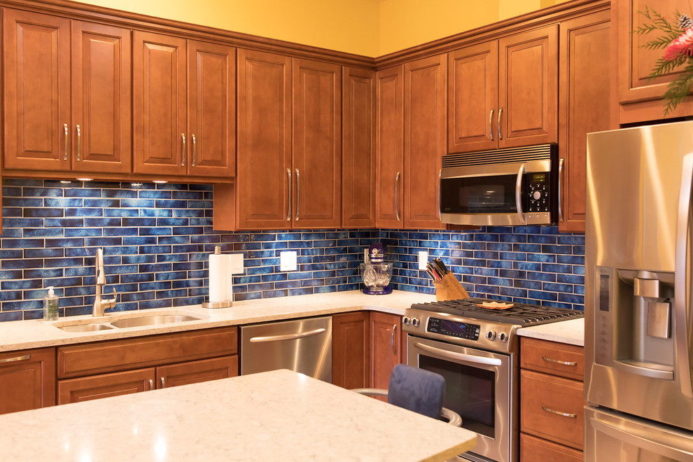 Klassisk inredning av ett mellanstort kök, med en undermonterad diskho, luckor med upphöjd panel, bruna skåp, bänkskiva i kvarts, blått stänkskydd, stänkskydd i porslinskakel, rostfria vitvaror, klinkergolv i keramik, en köksö och beiget golv