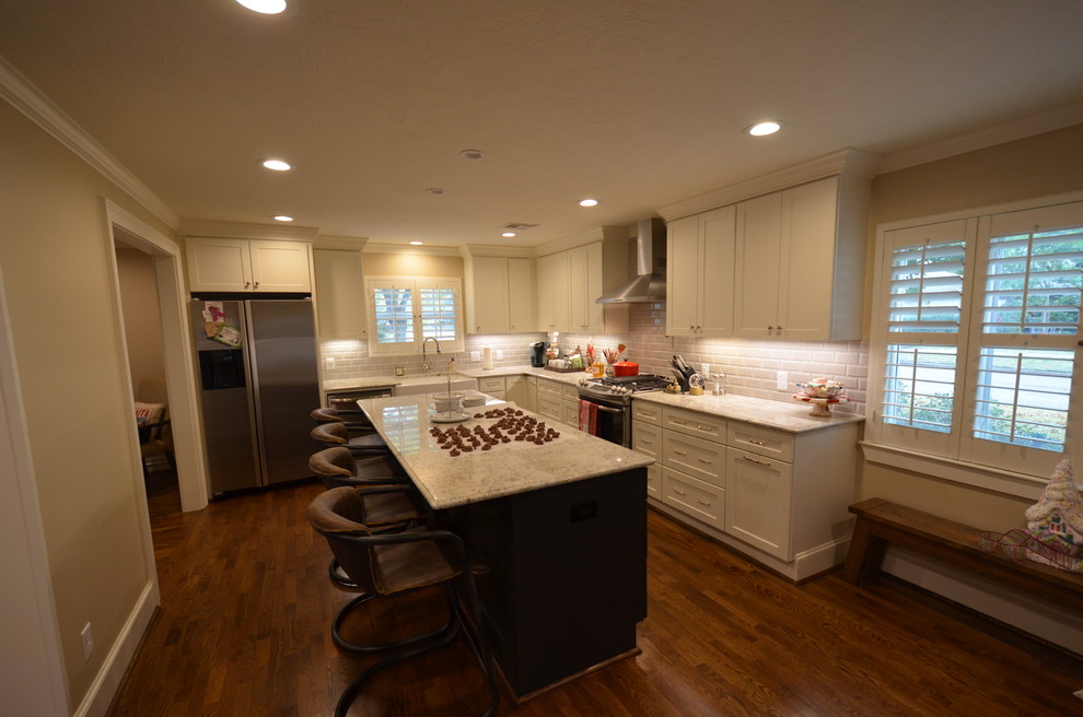 Amerikansk inredning av ett stort kök, med en rustik diskho, vita skåp, granitbänkskiva, grått stänkskydd, stänkskydd i porslinskakel, rostfria vitvaror, mellanmörkt trägolv, en köksö och skåp i shakerstil