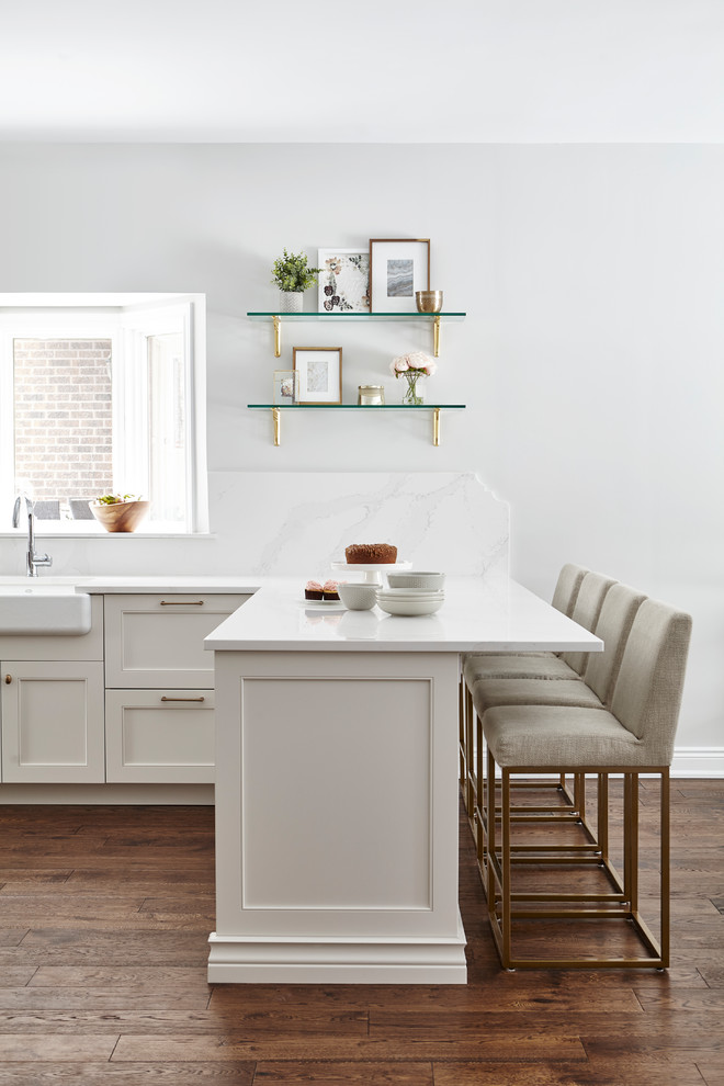 Bild på ett stort vintage vit vitt kök, med en rustik diskho, vita skåp, bänkskiva i kvarts, vitt stänkskydd, glaspanel som stänkskydd, rostfria vitvaror, mellanmörkt trägolv, en köksö och brunt golv