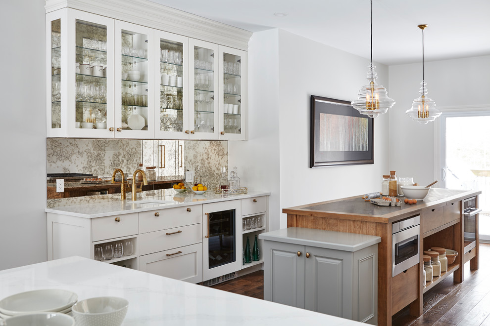 Klassisk inredning av ett stort vit vitt kök, med en rustik diskho, vita skåp, bänkskiva i kvarts, vitt stänkskydd, glaspanel som stänkskydd, rostfria vitvaror, mellanmörkt trägolv, en köksö och brunt golv