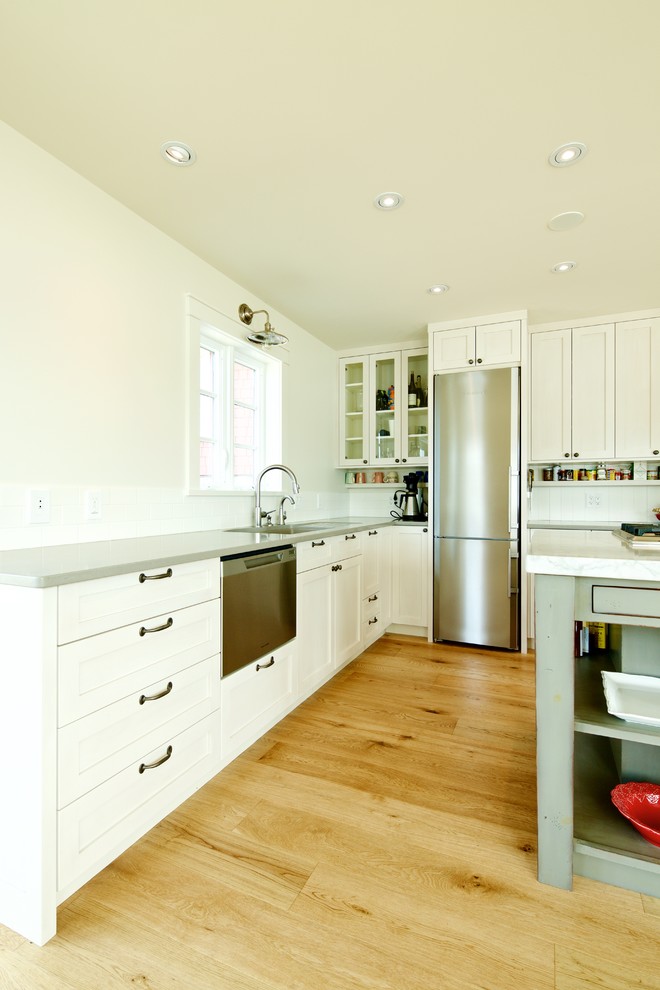 Bild på ett mellanstort eklektiskt kök, med en undermonterad diskho, skåp i shakerstil, vita skåp, bänkskiva i kvarts, vitt stänkskydd, rostfria vitvaror, ljust trägolv, en köksö och stänkskydd i tunnelbanekakel