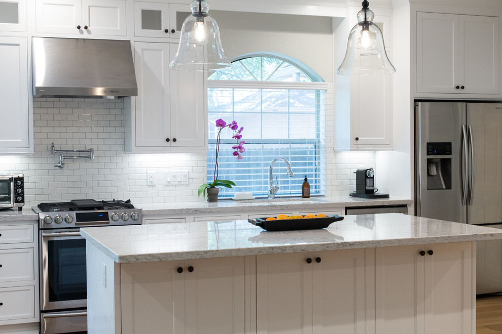 Mid-sized elegant l-shaped medium tone wood floor eat-in kitchen photo in Dallas with a single-bowl sink, recessed-panel cabinets, white cabinets, quartz countertops, white backsplash, subway tile backsplash, stainless steel appliances and an island