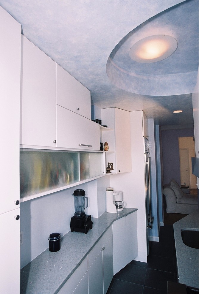 Cette photo montre une petite cuisine américaine parallèle moderne avec un évier encastré, un placard à porte plane, des portes de placard blanches, un plan de travail en quartz modifié, une crédence bleue, un électroménager en acier inoxydable, un sol en ardoise et aucun îlot.