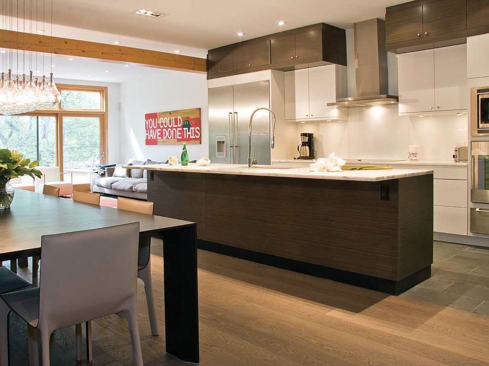 Diseño de cocina comedor lineal minimalista de tamaño medio con electrodomésticos de acero inoxidable, fregadero bajoencimera, armarios con paneles lisos, puertas de armario de madera en tonos medios, encimera de cuarzo compacto, salpicadero blanco, suelo de madera en tonos medios, una isla y encimeras blancas