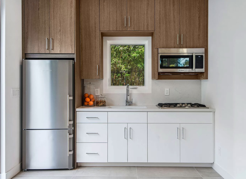 This is an example of a small contemporary single-wall open plan kitchen in Los Angeles with a submerged sink, flat-panel cabinets, white cabinets, white splashback, stainless steel appliances, no island, grey floors and white worktops.