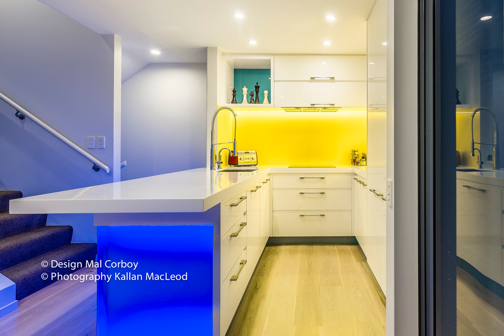 Bild på ett mellanstort funkis kök, med en undermonterad diskho, släta luckor, vita skåp, bänkskiva i koppar, gult stänkskydd, glaspanel som stänkskydd, vita vitvaror och ljust trägolv