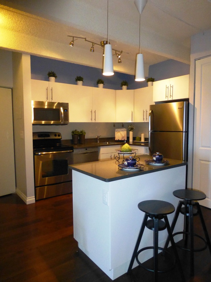 Exempel på ett litet modernt l-kök, med släta luckor, vita skåp, rostfria vitvaror, mörkt trägolv, en köksö och brunt golv