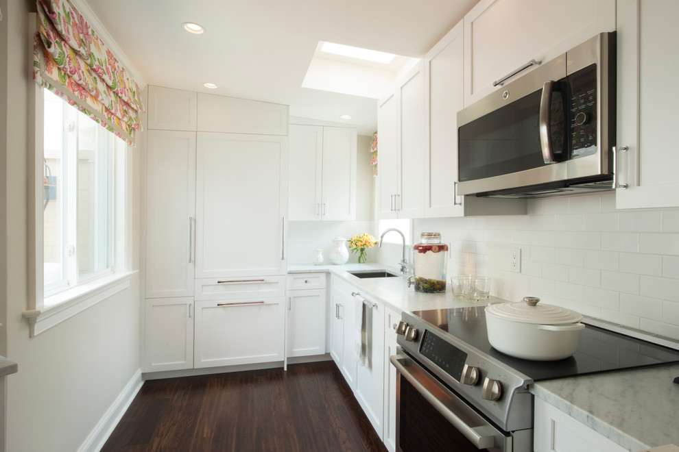 Exempel på ett litet klassiskt l-kök, med en undermonterad diskho, skåp i shakerstil, vita skåp, marmorbänkskiva, vitt stänkskydd, stänkskydd i tunnelbanekakel, integrerade vitvaror och mörkt trägolv
