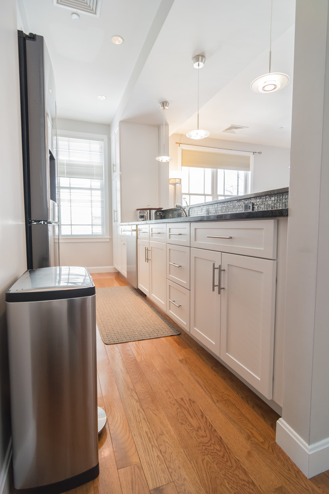 Mid-sized trendy galley medium tone wood floor and blue floor eat-in kitchen photo in Boston with an undermount sink, shaker cabinets, white cabinets, granite countertops, glass tile backsplash, stainless steel appliances, no island and gray backsplash