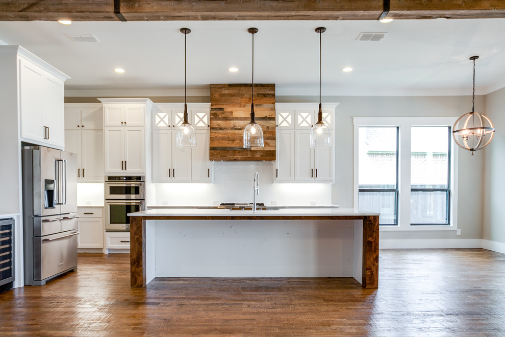 Foto på ett stort lantligt kök, med en undermonterad diskho, skåp i shakerstil, vita skåp, granitbänkskiva, vitt stänkskydd, stänkskydd i keramik, rostfria vitvaror, mellanmörkt trägolv, en köksö och brunt golv