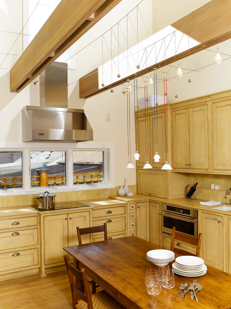 Imagen de cocina comedor de estilo de casa de campo con fregadero bajoencimera, armarios con paneles empotrados, puertas de armario de madera clara y electrodomésticos de acero inoxidable