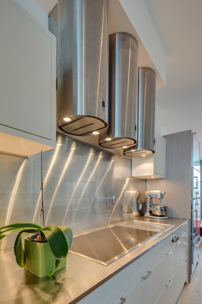 Immagine di una cucina minimal di medie dimensioni con ante lisce, ante beige, paraspruzzi a effetto metallico, paraspruzzi con piastrelle di metallo, elettrodomestici in acciaio inossidabile, parquet chiaro, pavimento marrone e top grigio