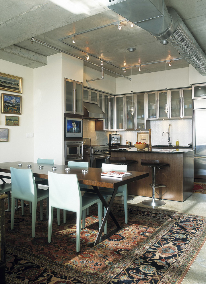Modern inredning av ett kök och matrum, med rostfria vitvaror, luckor med glaspanel, skåp i rostfritt stål och vitt stänkskydd