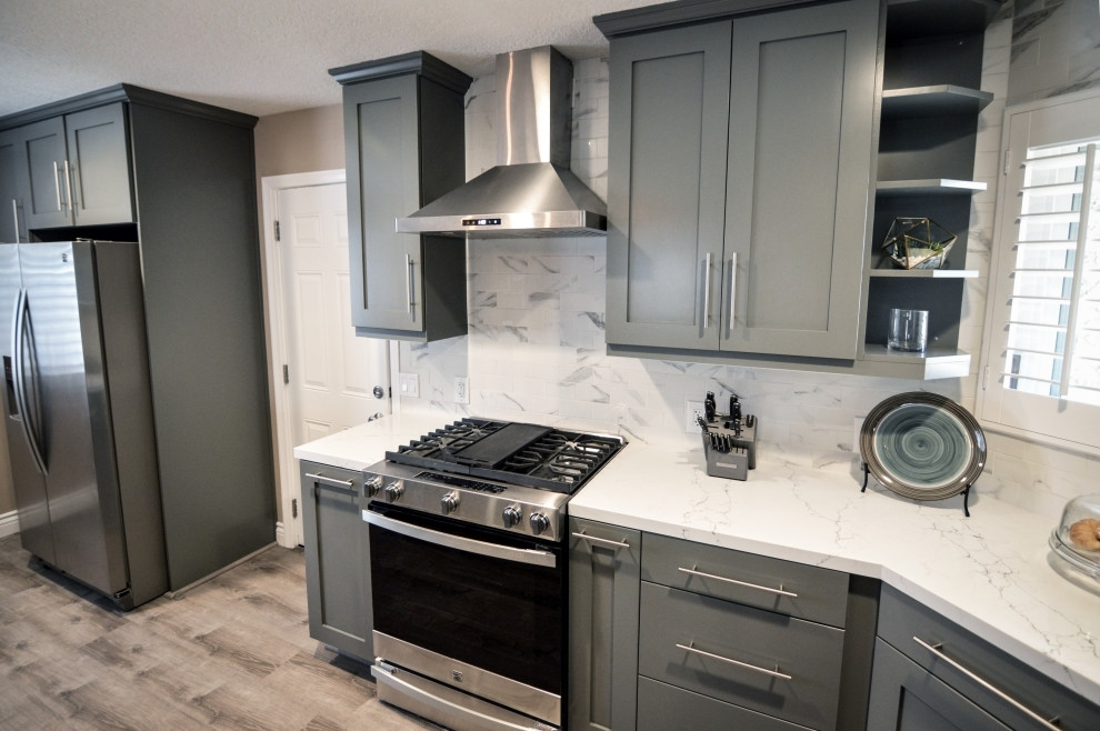 Foto på ett stort funkis vit linjärt kök och matrum, med en undermonterad diskho, skåp i shakerstil, grå skåp, bänkskiva i kvarts, grått stänkskydd, stänkskydd i porslinskakel, rostfria vitvaror, ljust trägolv och en köksö
