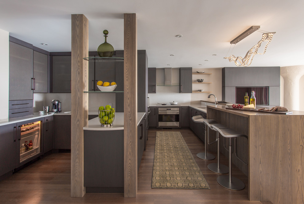 Cette photo montre une cuisine tendance avec un placard à porte plane, des portes de placard grises, une crédence blanche, un électroménager en acier inoxydable et un sol en bois brun.