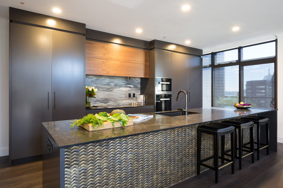 Large contemporary galley open plan kitchen in Auckland with flat-panel cabinets, black cabinets, engineered stone countertops, multi-coloured splashback, stainless steel appliances and an island.