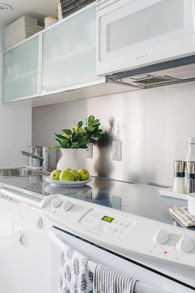 Photo of a small traditional galley kitchen/diner in Toronto with a built-in sink, flat-panel cabinets, white cabinets, granite worktops, metallic splashback, metal splashback, white appliances, dark hardwood flooring and no island.