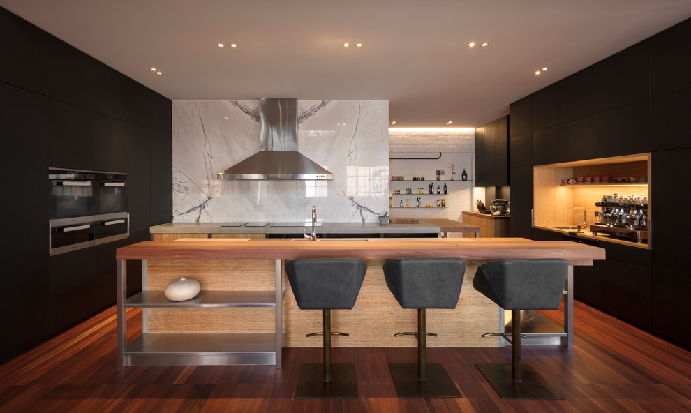 This is an example of a large contemporary u-shaped kitchen/diner in Melbourne with a submerged sink, flat-panel cabinets, black cabinets, concrete worktops, white splashback, marble splashback, stainless steel appliances, medium hardwood flooring, an island, brown floors and grey worktops.