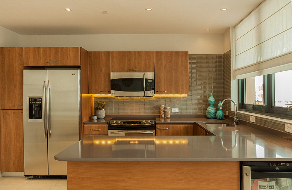 This is an example of a medium sized contemporary u-shaped open plan kitchen in Other with a breakfast bar, flat-panel cabinets, medium wood cabinets, engineered stone countertops, grey splashback, glass tiled splashback, stainless steel appliances, a submerged sink and porcelain flooring.