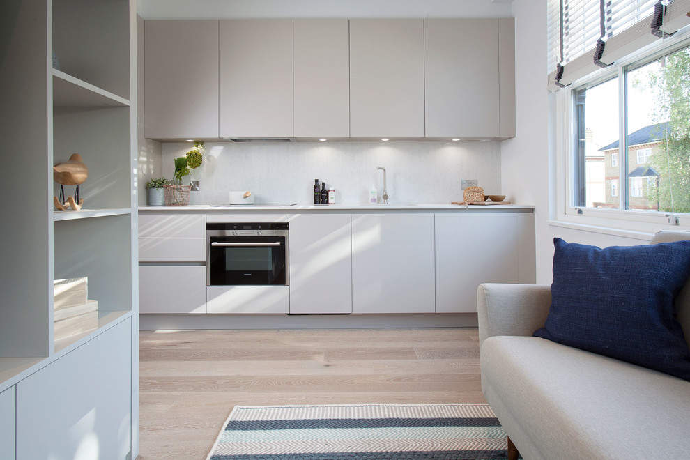 Nordische Küche mit flächenbündigen Schrankfronten, grauen Schränken, Küchenrückwand in Grau und hellem Holzboden in London