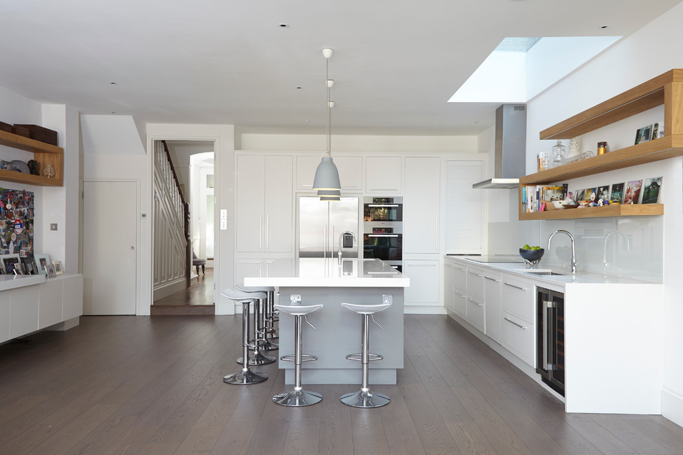 Moderne Küche in L-Form mit Unterbauwaschbecken, flächenbündigen Schrankfronten, weißen Schränken, Küchenrückwand in Weiß, Glasrückwand, Küchengeräten aus Edelstahl, braunem Holzboden und Kücheninsel in London