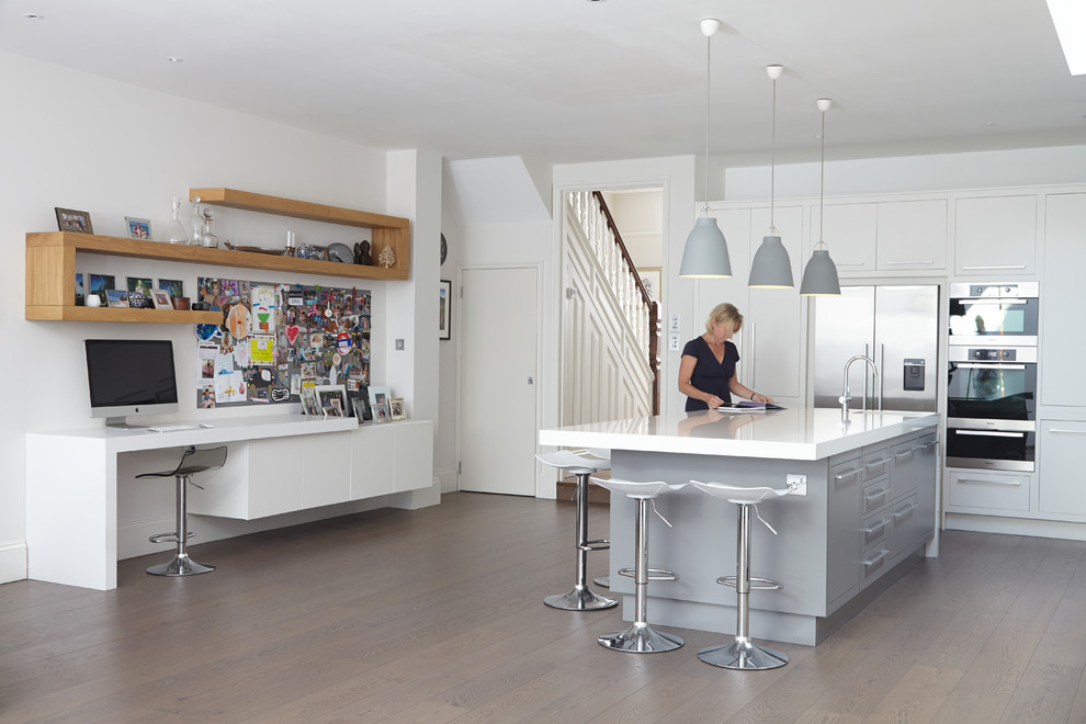 Bild på ett funkis kök, med en undermonterad diskho, släta luckor, vita skåp, rostfria vitvaror, mellanmörkt trägolv och en köksö