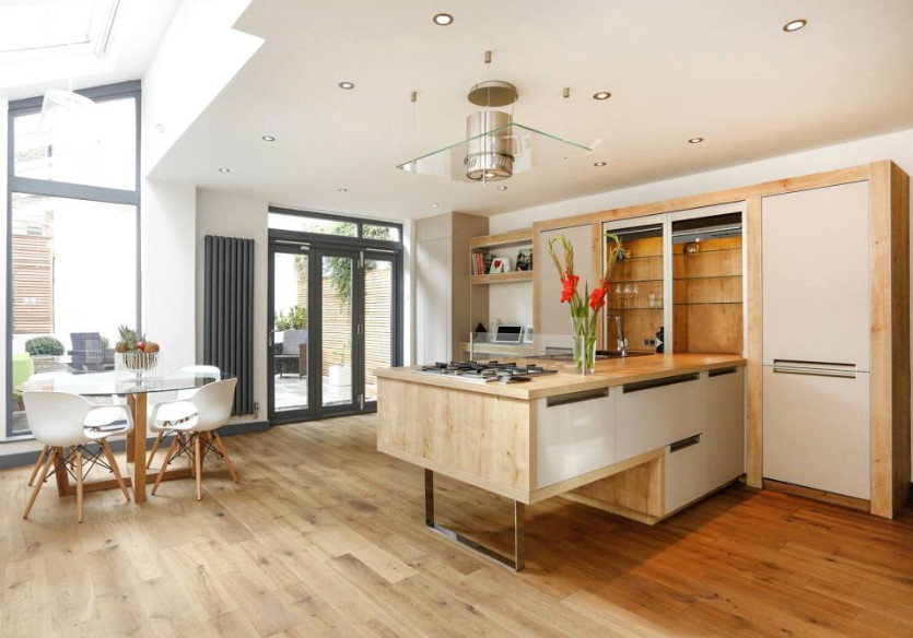 This is an example of a traditional kitchen/diner in London with flat-panel cabinets, grey cabinets, wood worktops, light hardwood flooring and an island.