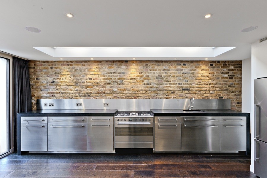 Example of a mid-sized trendy single-wall dark wood floor eat-in kitchen design in London with a single-bowl sink, flat-panel cabinets, stainless steel cabinets, granite countertops, metallic backsplash, stainless steel appliances and no island