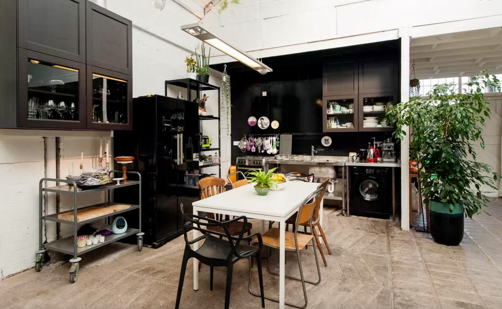This is an example of a medium sized industrial open plan kitchen in London with a submerged sink, glass-front cabinets, grey cabinets, stainless steel worktops, black appliances, no island and grey floors.