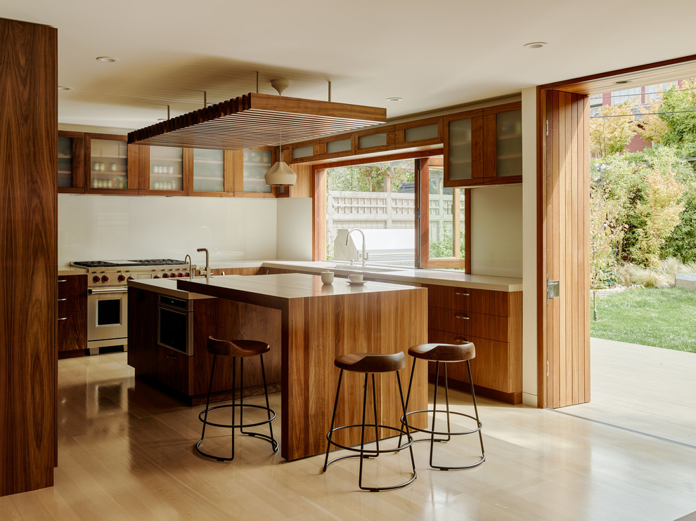 Moderne Küche mit hellbraunen Holzschränken, Küchenrückwand in Weiß, Küchengeräten aus Edelstahl, hellem Holzboden und zwei Kücheninseln in San Francisco