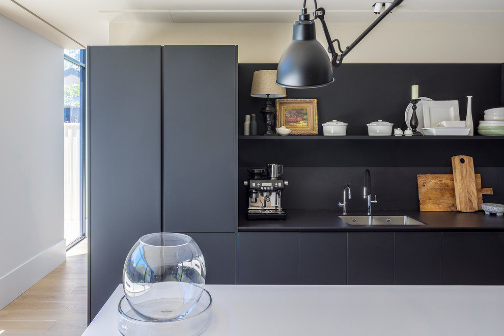 This is an example of a large contemporary l-shaped open plan kitchen in Perth with dark wood cabinets, composite countertops, black splashback, black appliances, light hardwood flooring, an island and white worktops.