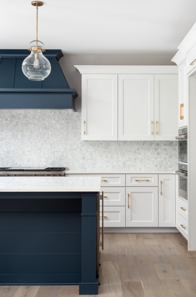 This is an example of a large country u-shaped open plan kitchen in Chicago with a belfast sink, recessed-panel cabinets, white cabinets, multi-coloured splashback, stainless steel appliances, an island, beige floors and light hardwood flooring.