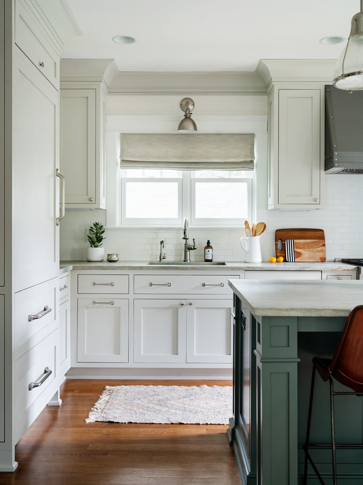 Inspiration for a mid-sized transitional l-shaped medium tone wood floor open concept kitchen remodel in New York with a drop-in sink, shaker cabinets, white cabinets, white backsplash, subway tile backsplash, stainless steel appliances, an island and white countertops