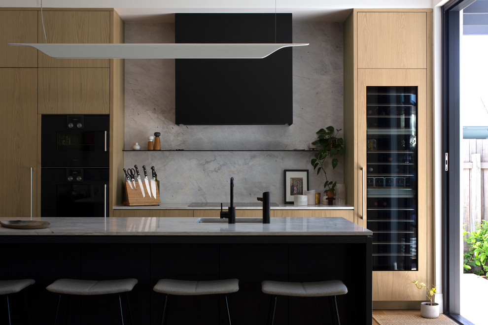 Contemporary galley open plan kitchen in Perth with a single-bowl sink, flat-panel cabinets, light wood cabinets, marble worktops, grey splashback, marble splashback, black appliances, light hardwood flooring, an island and grey worktops.