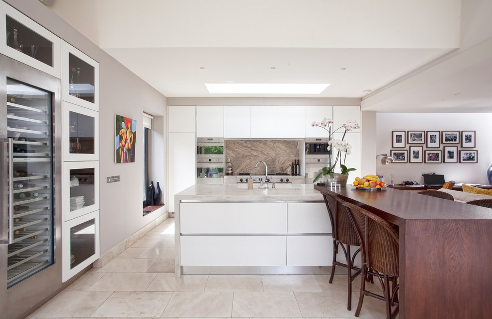 Photo of a contemporary galley open plan kitchen in Dublin with flat-panel cabinets, white cabinets, brown splashback and stone slab splashback.