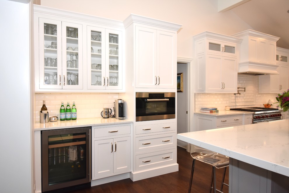 Foto på ett mycket stort vintage vit kök med öppen planlösning, med en enkel diskho, skåp i shakerstil, vita skåp, bänkskiva i kvarts, vitt stänkskydd, stänkskydd i keramik, rostfria vitvaror, mellanmörkt trägolv, flera köksöar och brunt golv