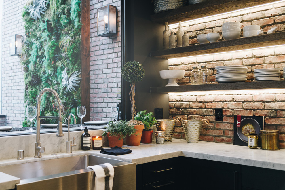 Photo of a large industrial u-shaped kitchen/diner in Los Angeles with a belfast sink, shaker cabinets, black cabinets, red splashback, brick splashback, stainless steel appliances, laminate floors, an island, brown floors and white worktops.