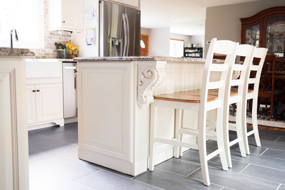 Bild på ett litet lantligt kök, med en rustik diskho, luckor med upphöjd panel, vita skåp, granitbänkskiva, flerfärgad stänkskydd, stänkskydd i stenkakel, rostfria vitvaror, cementgolv, en köksö och grått golv