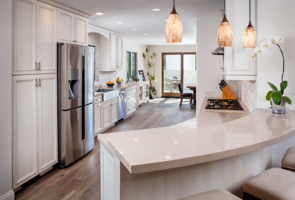 Photo of a large mediterranean galley kitchen/diner in San Diego with a belfast sink, beaded cabinets, beige cabinets, limestone worktops, beige splashback, stone tiled splashback, stainless steel appliances, medium hardwood flooring and a breakfast bar.