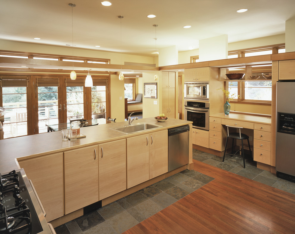 Cette image montre une cuisine américaine design en L et bois brun avec un évier posé, un placard à porte plane, un plan de travail en stratifié, une crédence grise et un électroménager en acier inoxydable.