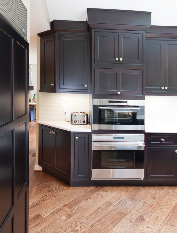 Exempel på ett stort amerikanskt kök, med en undermonterad diskho, luckor med profilerade fronter, skåp i mörkt trä, bänkskiva i glas, beige stänkskydd, stänkskydd i cementkakel, rostfria vitvaror, mellanmörkt trägolv och en köksö