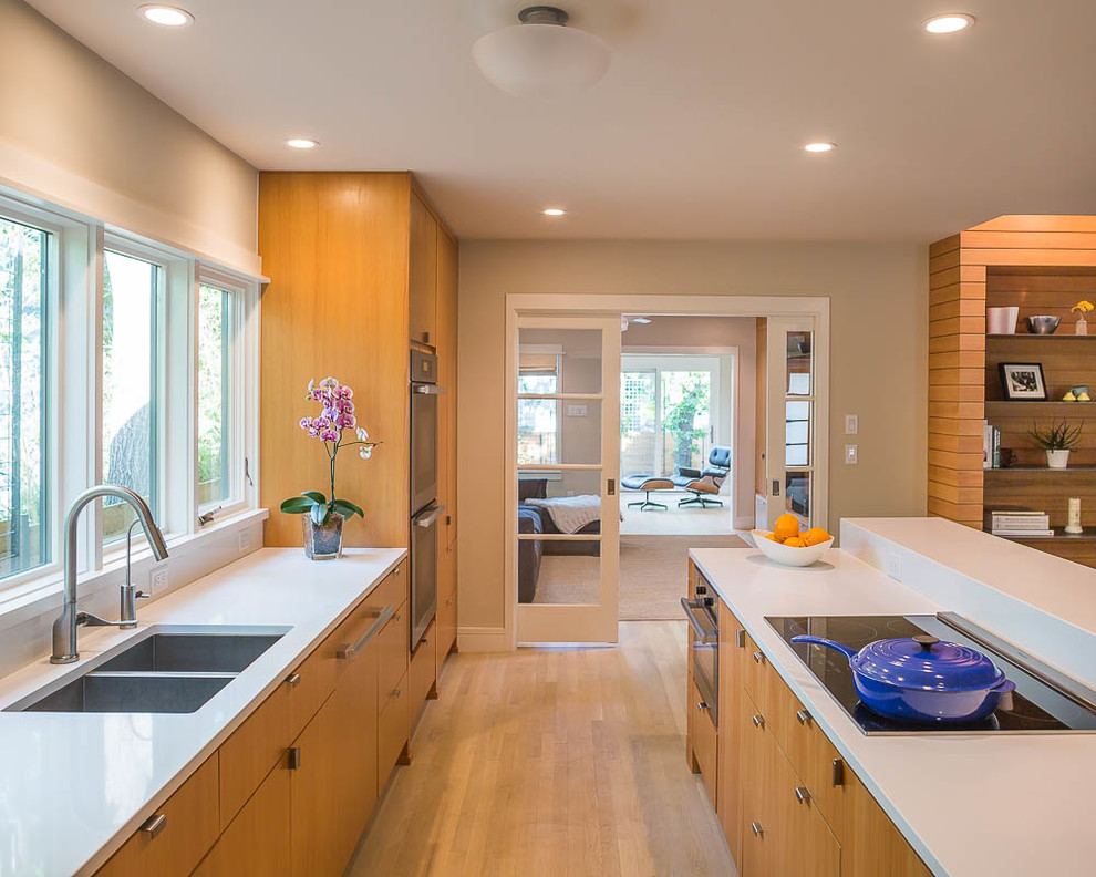 Moderne Küche mit Doppelwaschbecken, flächenbündigen Schrankfronten, hellbraunen Holzschränken, braunem Holzboden und Kücheninsel in Austin