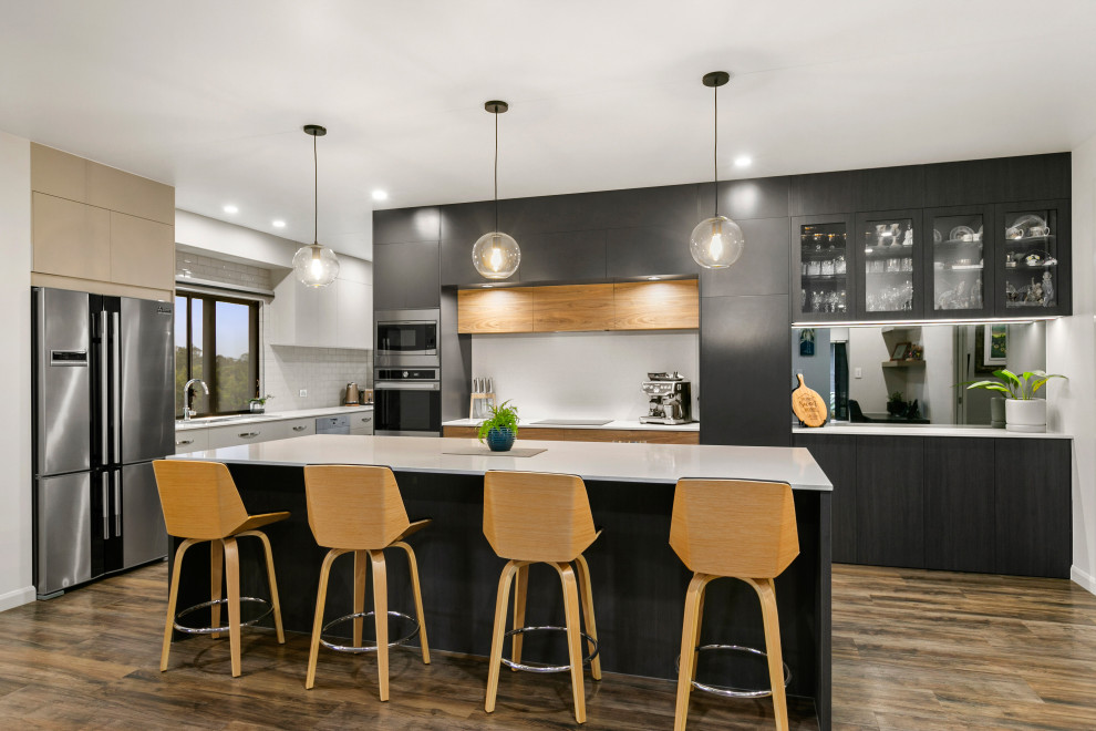 Moderne Küche mit Einbauwaschbecken, flächenbündigen Schrankfronten, schwarzen Schränken, Küchenrückwand in Weiß, Rückwand aus Spiegelfliesen, braunem Holzboden, Kücheninsel, braunem Boden und gelber Arbeitsplatte in Sonstige