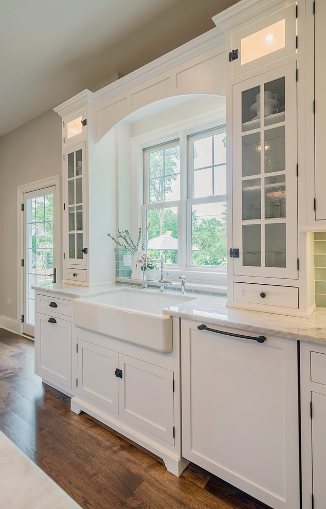 Eat-in kitchen - mid-sized transitional l-shaped medium tone wood floor eat-in kitchen idea in Chicago with a farmhouse sink, shaker cabinets, white cabinets, quartzite countertops, green backsplash, ceramic backsplash, paneled appliances and an island